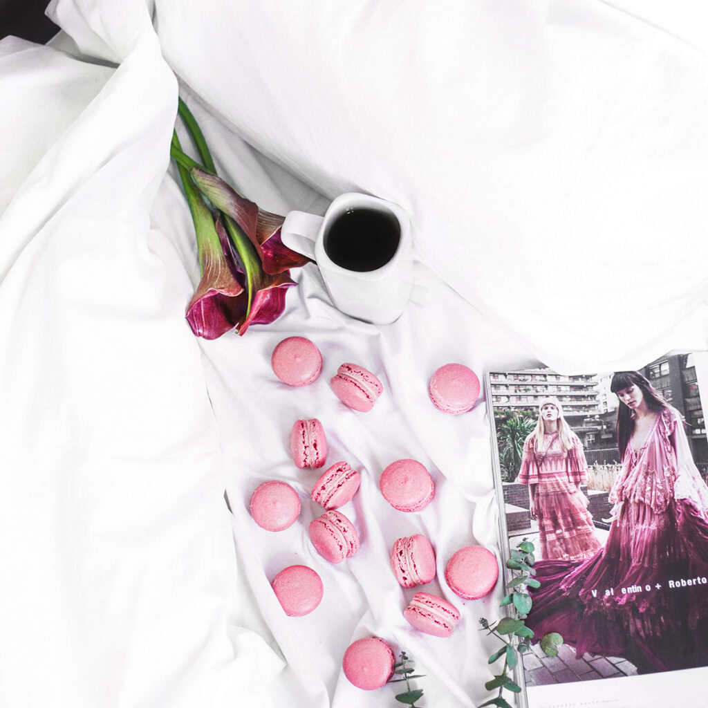 A mug of coffee, pink flowers, and a magazine over a white background