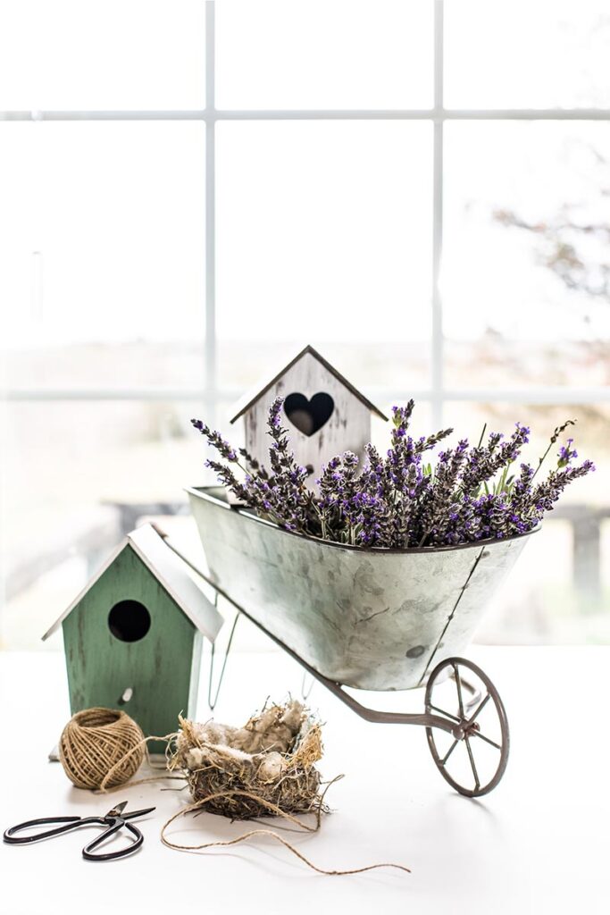 Two decorative birdhouses and a wheelbarrow with purple flowers
